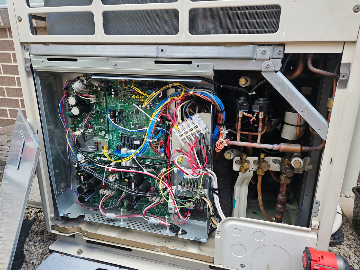 Outdoor air conditioning unit opened for diagnostics, showing circuit boards and copper pipework
